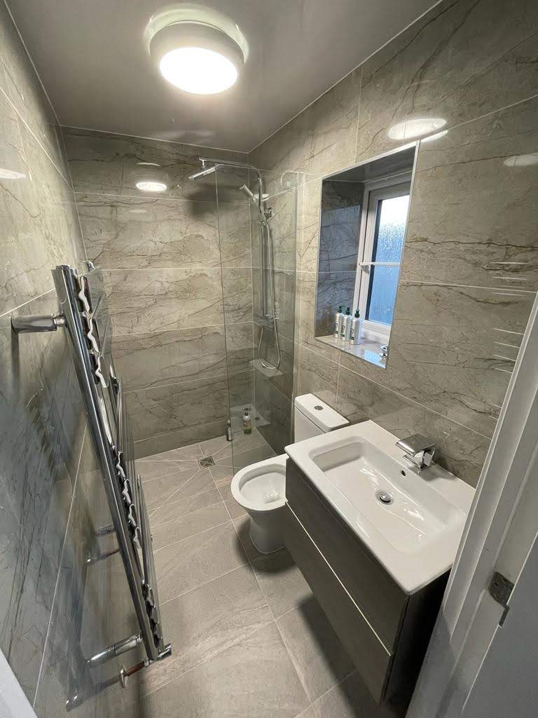 A compact wet room with marble-effect wall tiles, a wall-hung basin and a heated towel rail