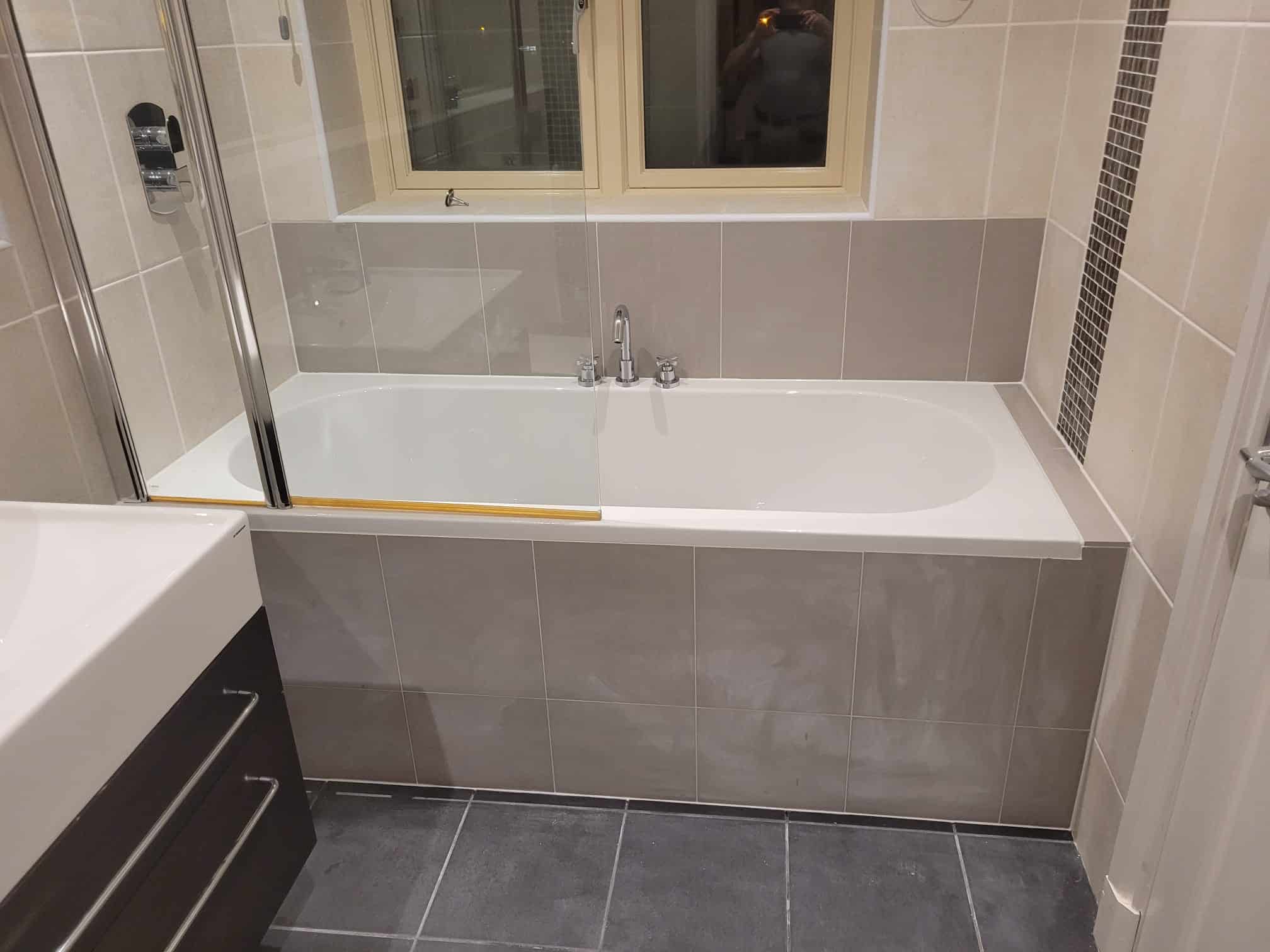 A tiled bath with a glass screen, chrome mixer taps and a dark vanity unit