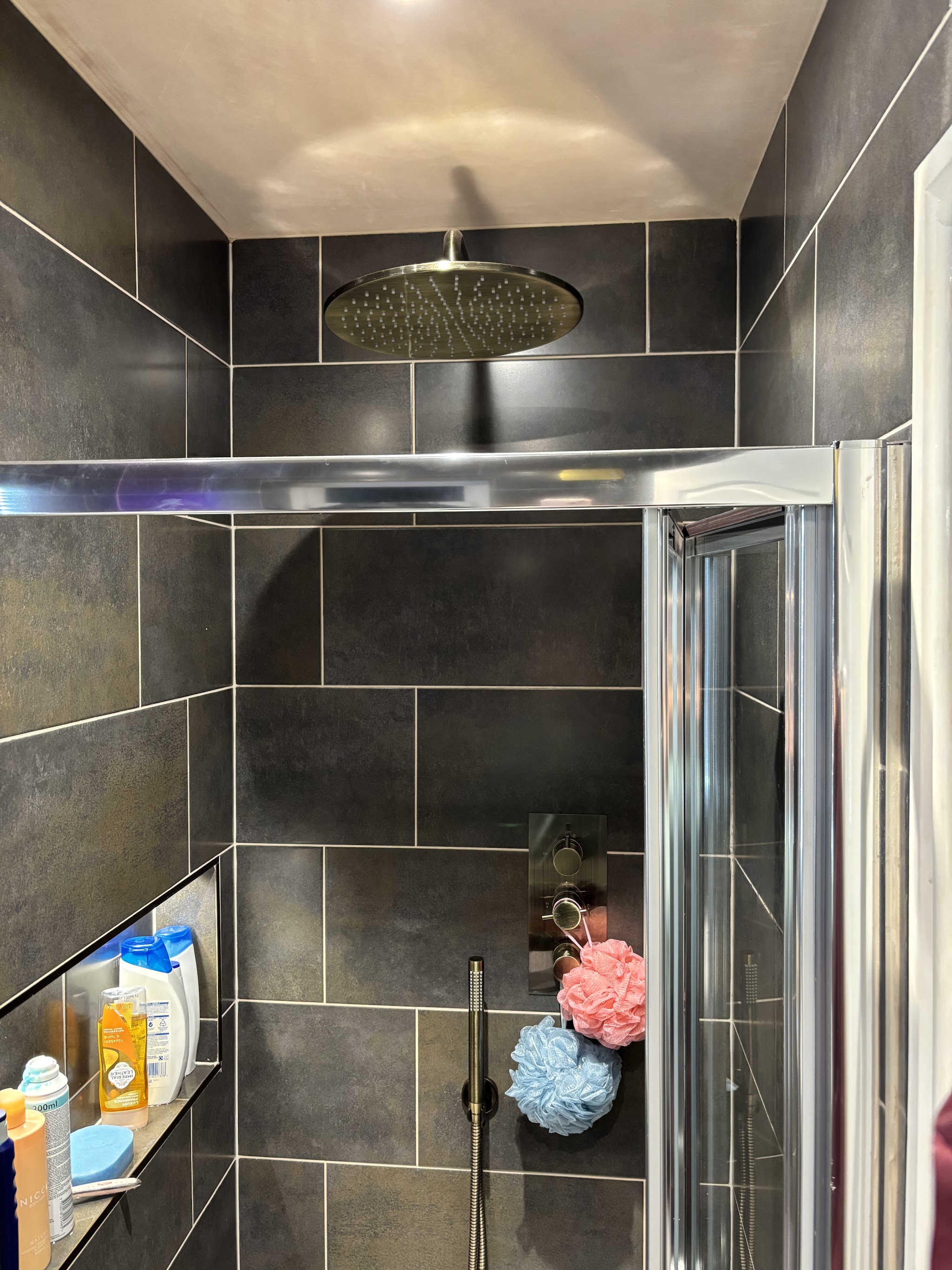A dark-tiled shower with a brushed brass rain head and thermostatic valve