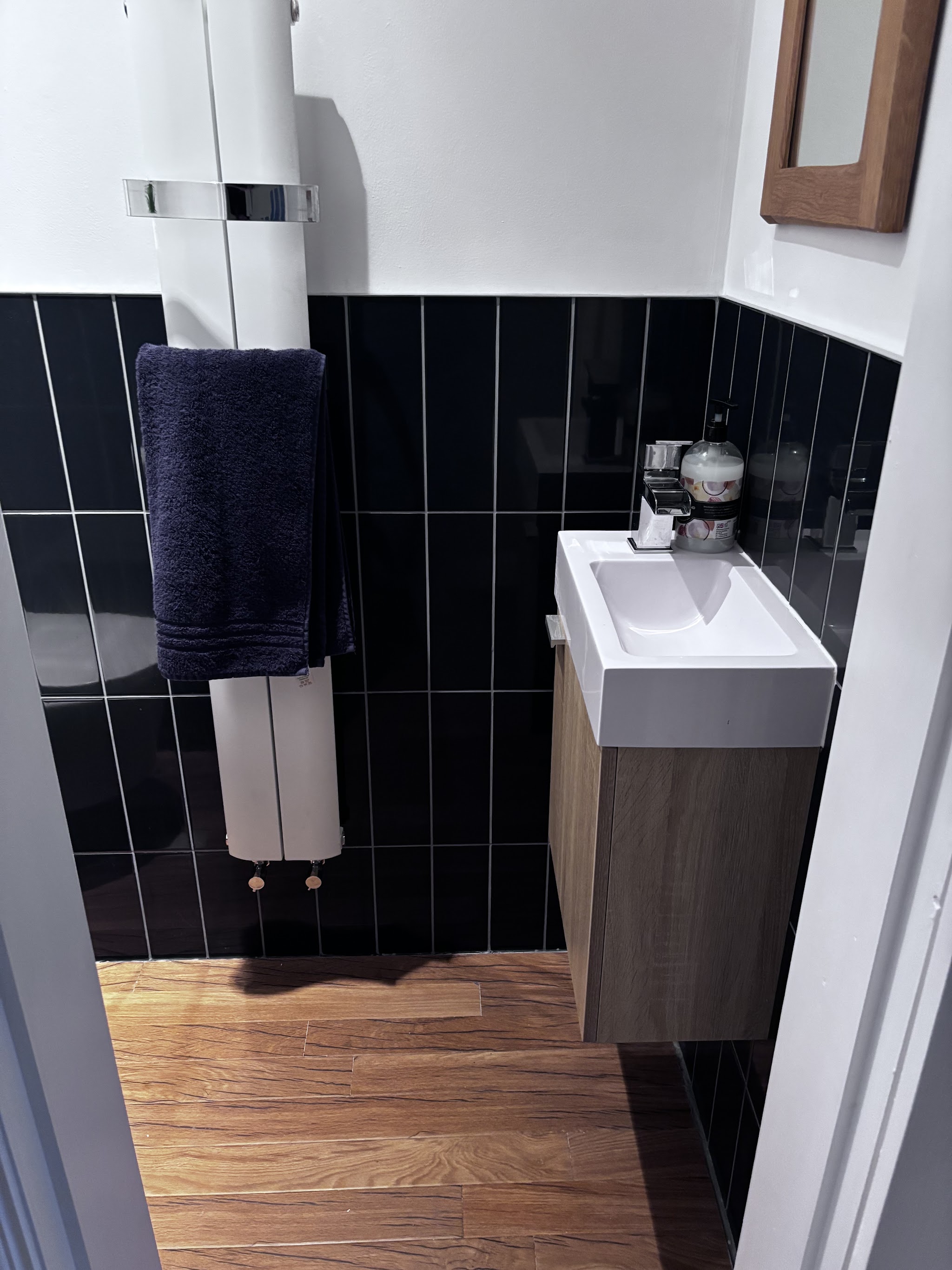 A cloakroom with dark vertical wall tiles, a small basin unit and a white towel radiator